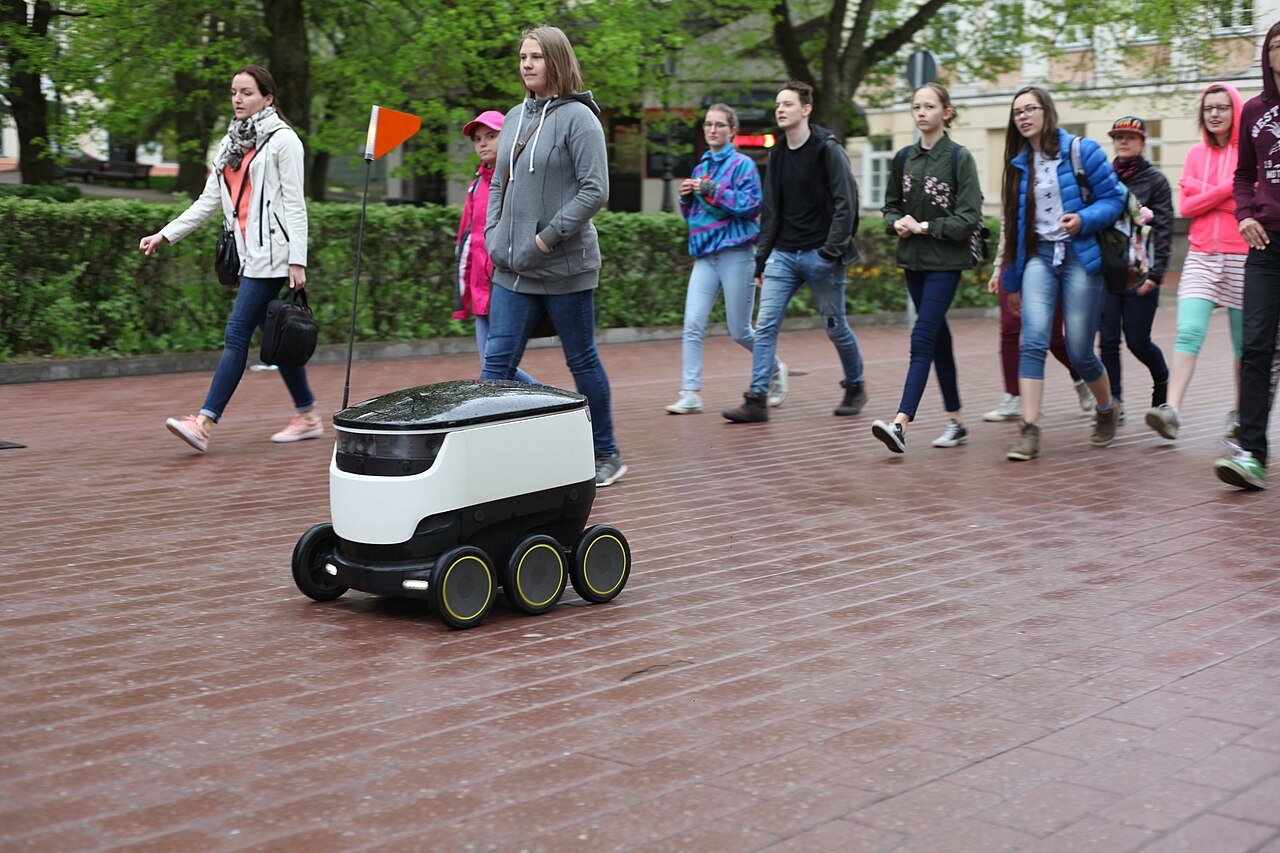 A Starship delivery robot rolling across a brick plaza among pedestrians
