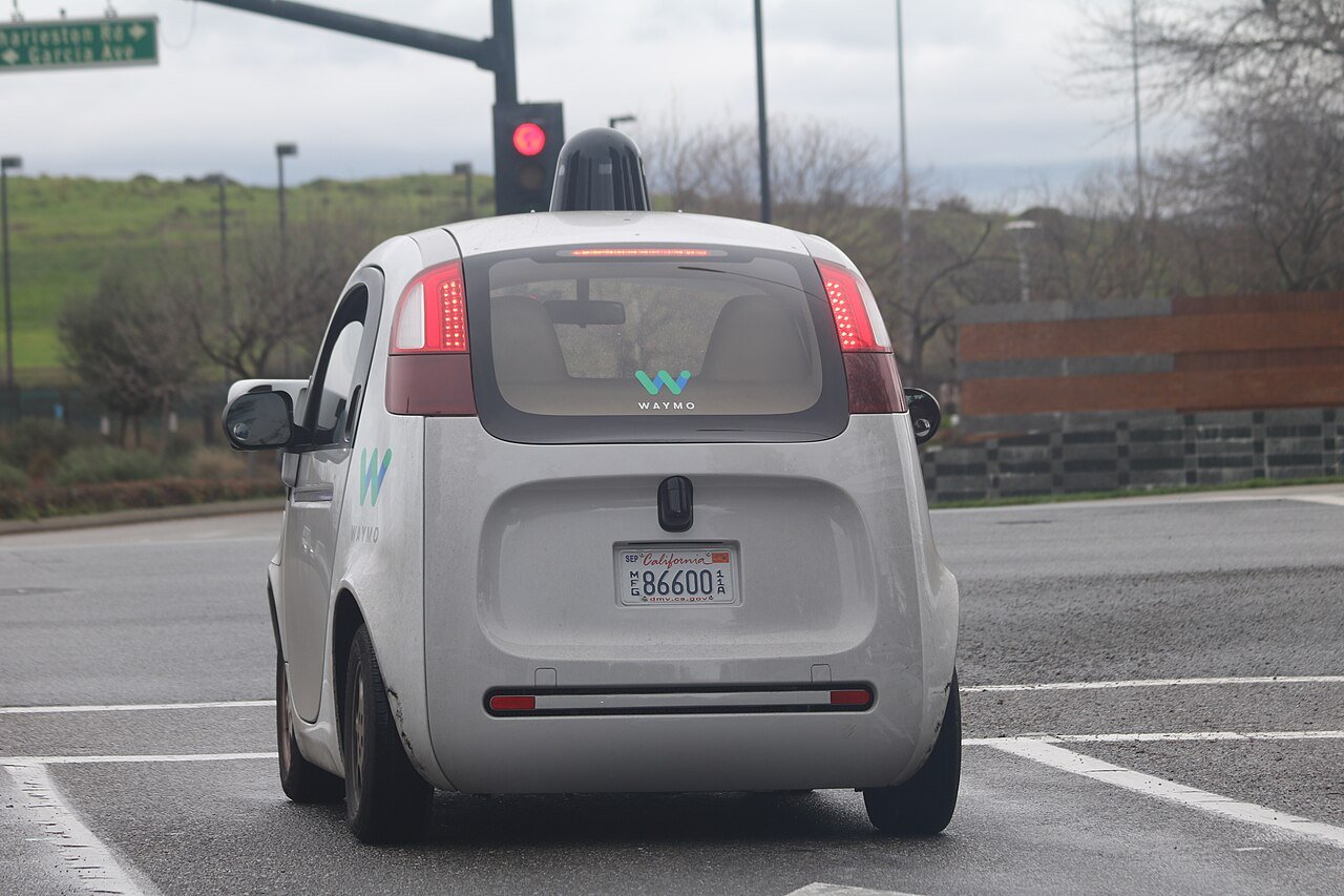 A Waymo self-driving car with roof sensor dome waiting at a red light